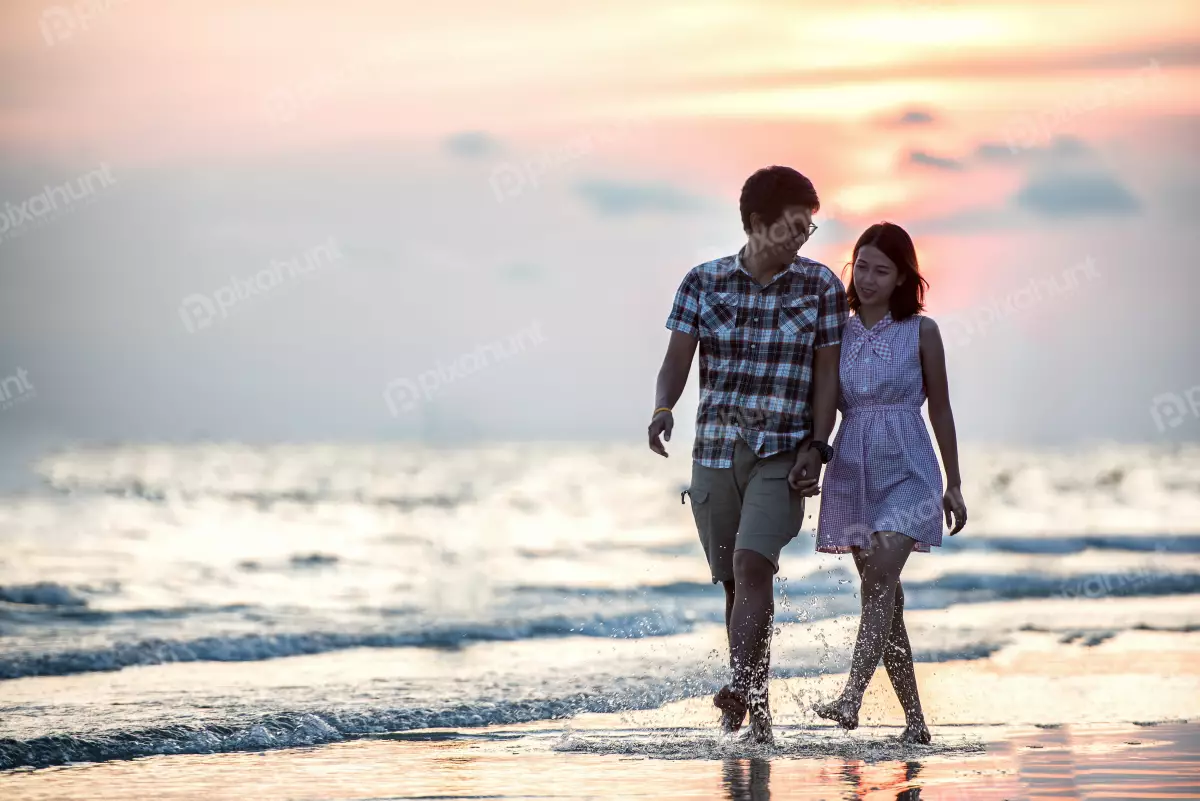Free Premium Stock Photos A beautiful  couple sunset on the beach walking hand-in-hand along the shore and the waves are gently lapping at their feet