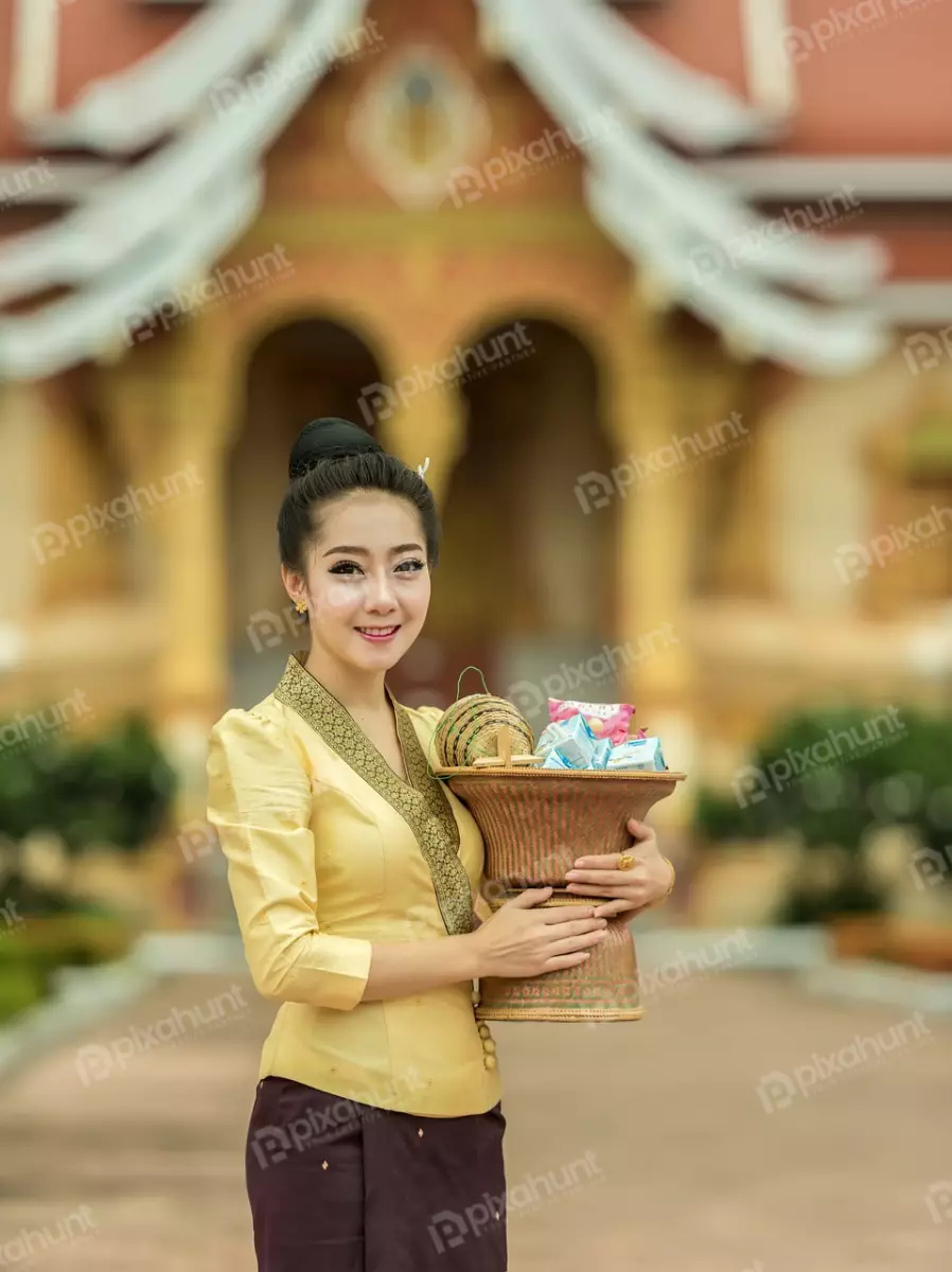 Free Premium Stock Photos A beautiful young woman dressed in a traditional Thai outfit and standing in front of a temple, with a golden bowl in her hands