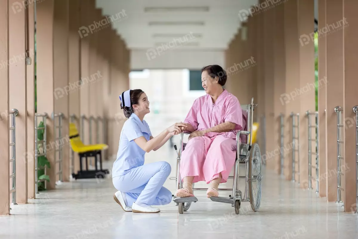 Free Premium Stock Photos A nurse kneeling next to a patient in a wheelchair and nurse is smiling and holding the patient's hand