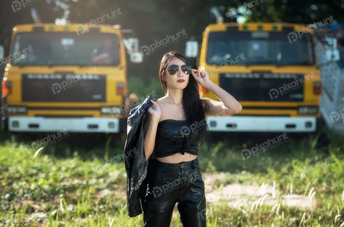 Free Premium Stock Photos A woman in a black leather jacket and sunglasses stands in front of two yellow trucks And looking at the camera and has one hand on her hip and the other holding her jacket