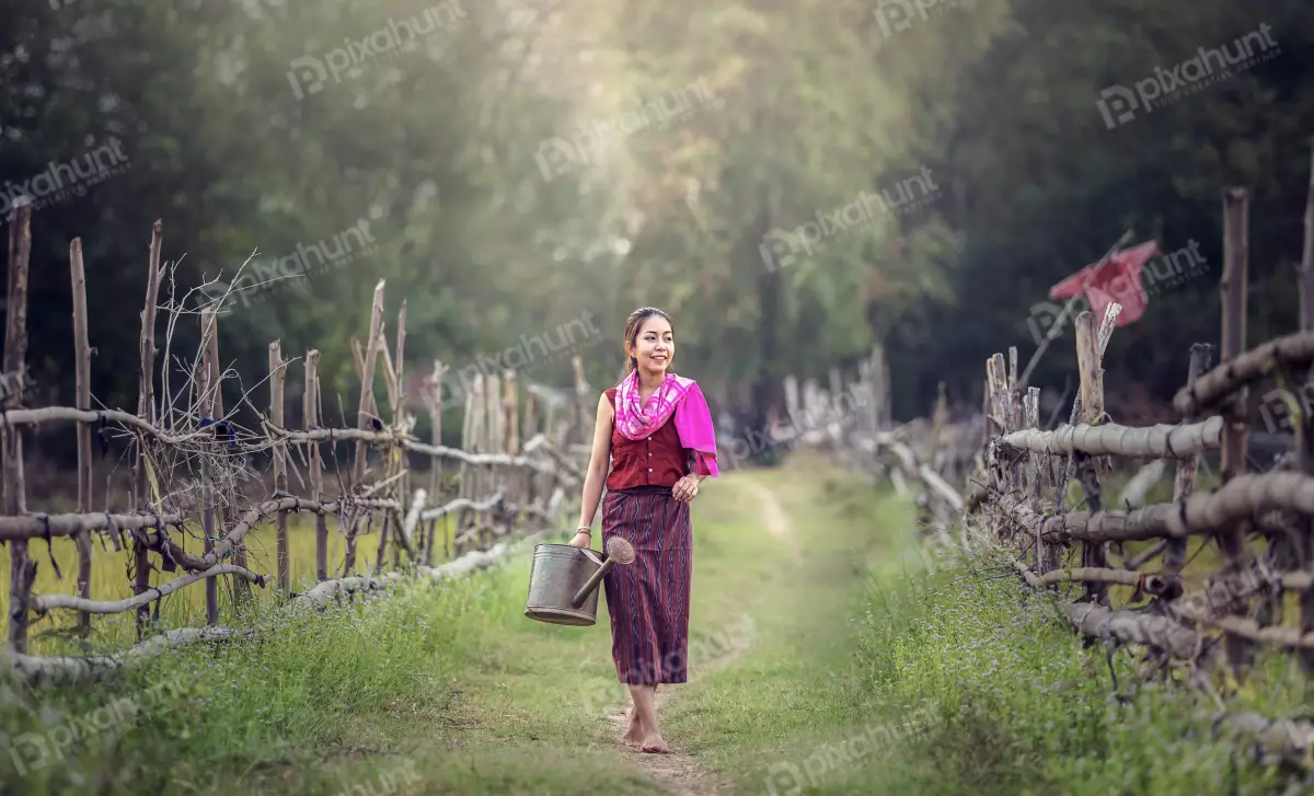 Free Premium Stock Photos A woman in a traditional Hmong outfit and walking down a path in a rural area carrying a watering can