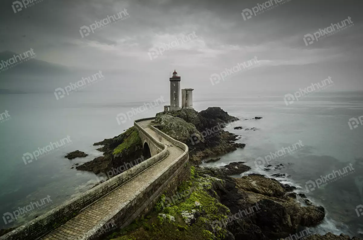 Free Premium Stock Photos looking down on a lighthouse is in the center of the photo, and a long, curved stone jetty leads up to it