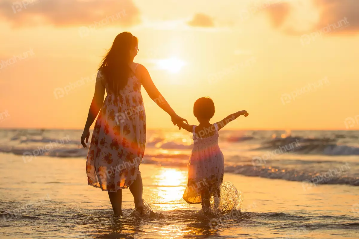 Free Premium Stock Photos looking up at a mother and her daughter as they walk hand-in-hand along a beach at sunset