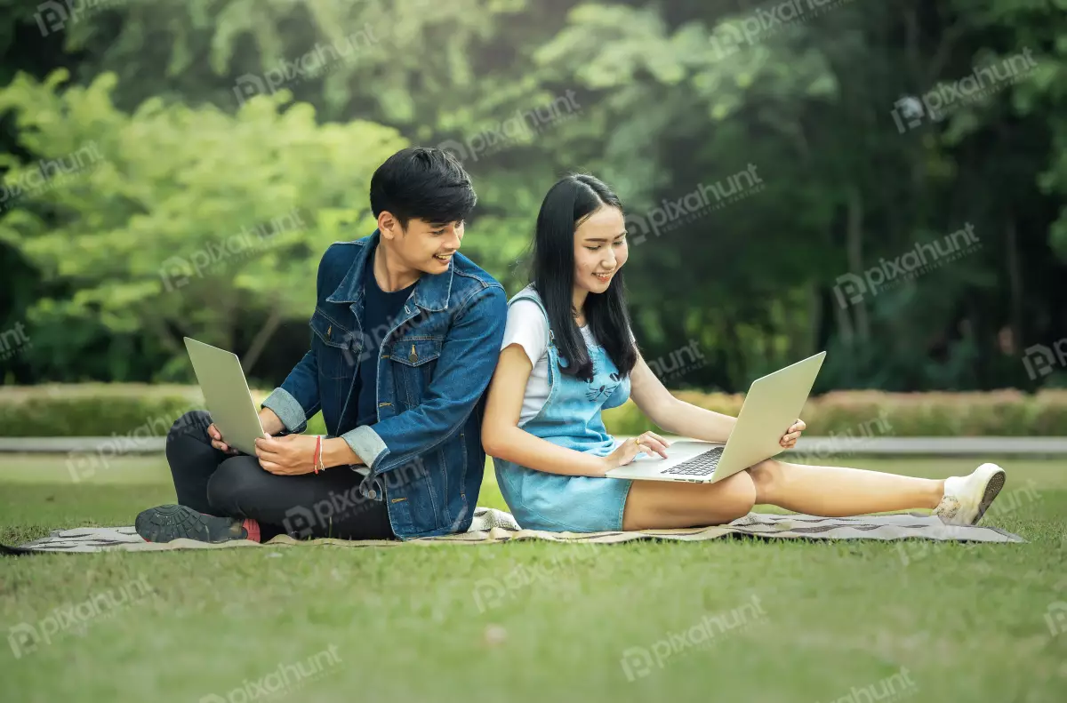 Free Premium Stock Photos Student sitting on the grass in a park and man is sitting with his back to the woman and they are both looking at their laptops