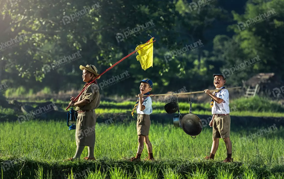 Free Premium Stock Photos Three boy scouts in a field and boy in the middle is holding a flag, the boy on the left is holding a lantern and the boy on the right is carrying a pot.