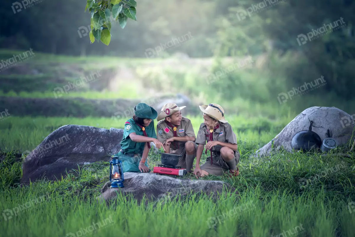 Free Premium Stock Photos Three boy scouts in a forest and gathered around a campfire and one of them is stirring a pot of food