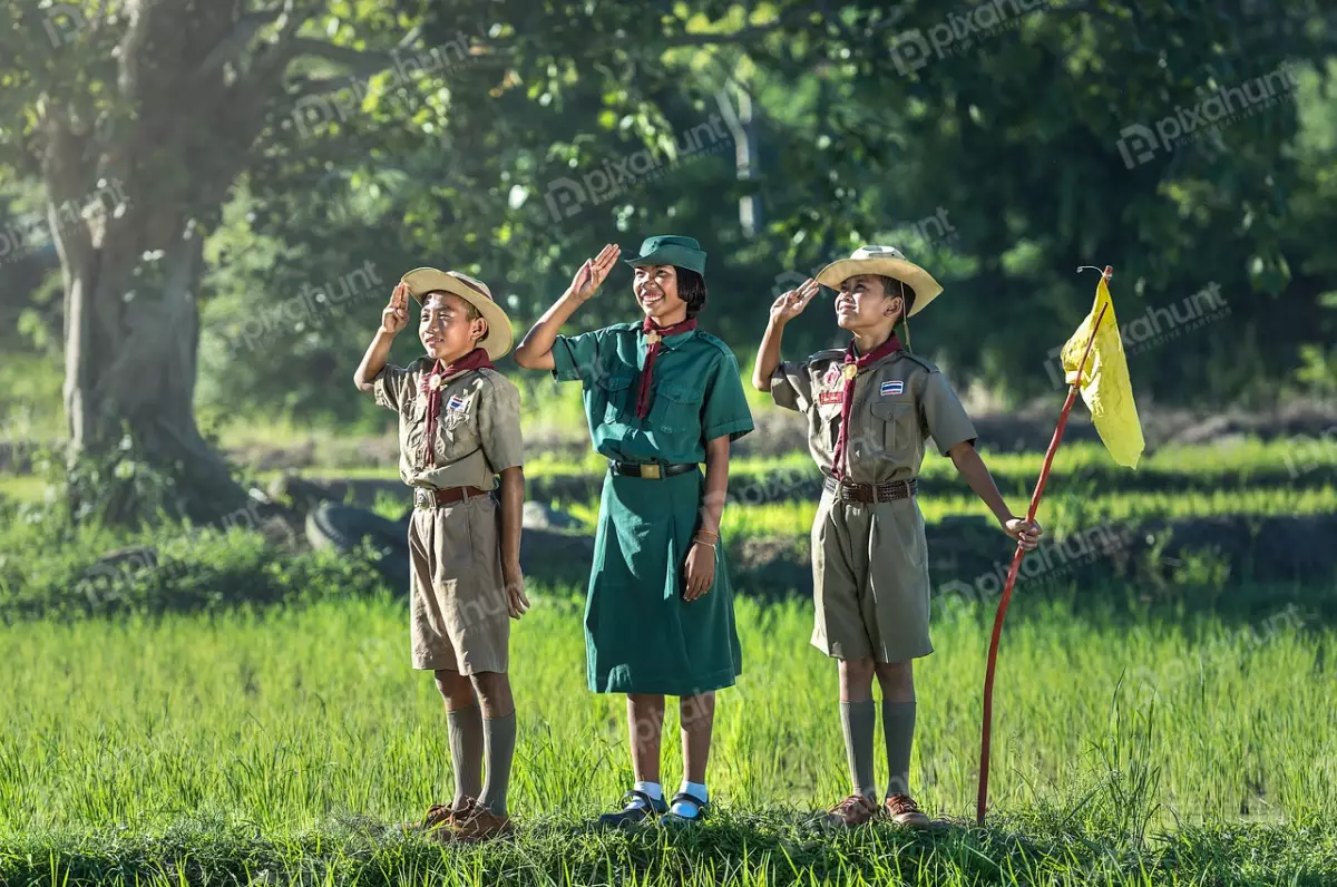 Free Premium Stock Photos Three scouts in a field, saluting and two boys are wearing brown uniforms, and the girl is wearing a green uniform