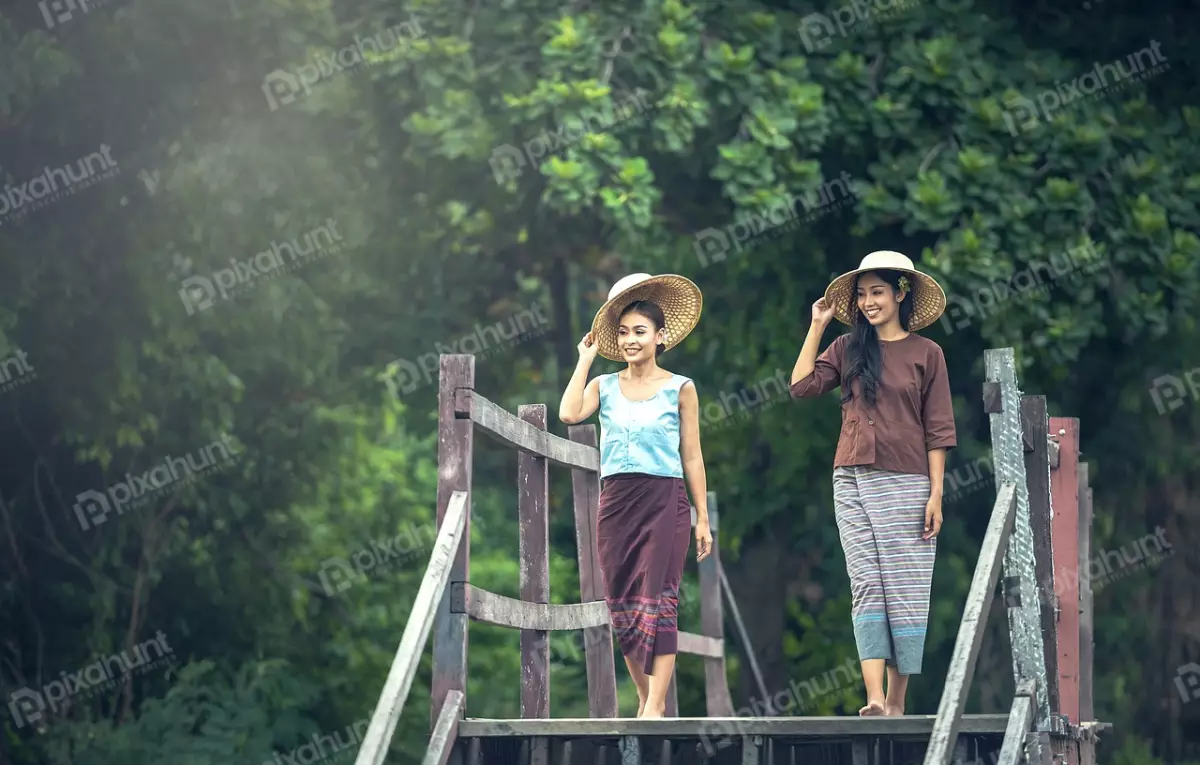 Free Premium Stock Photos Two beautiful young women in traditional Thai clothing walking on a wooden bridge in a lush green forest