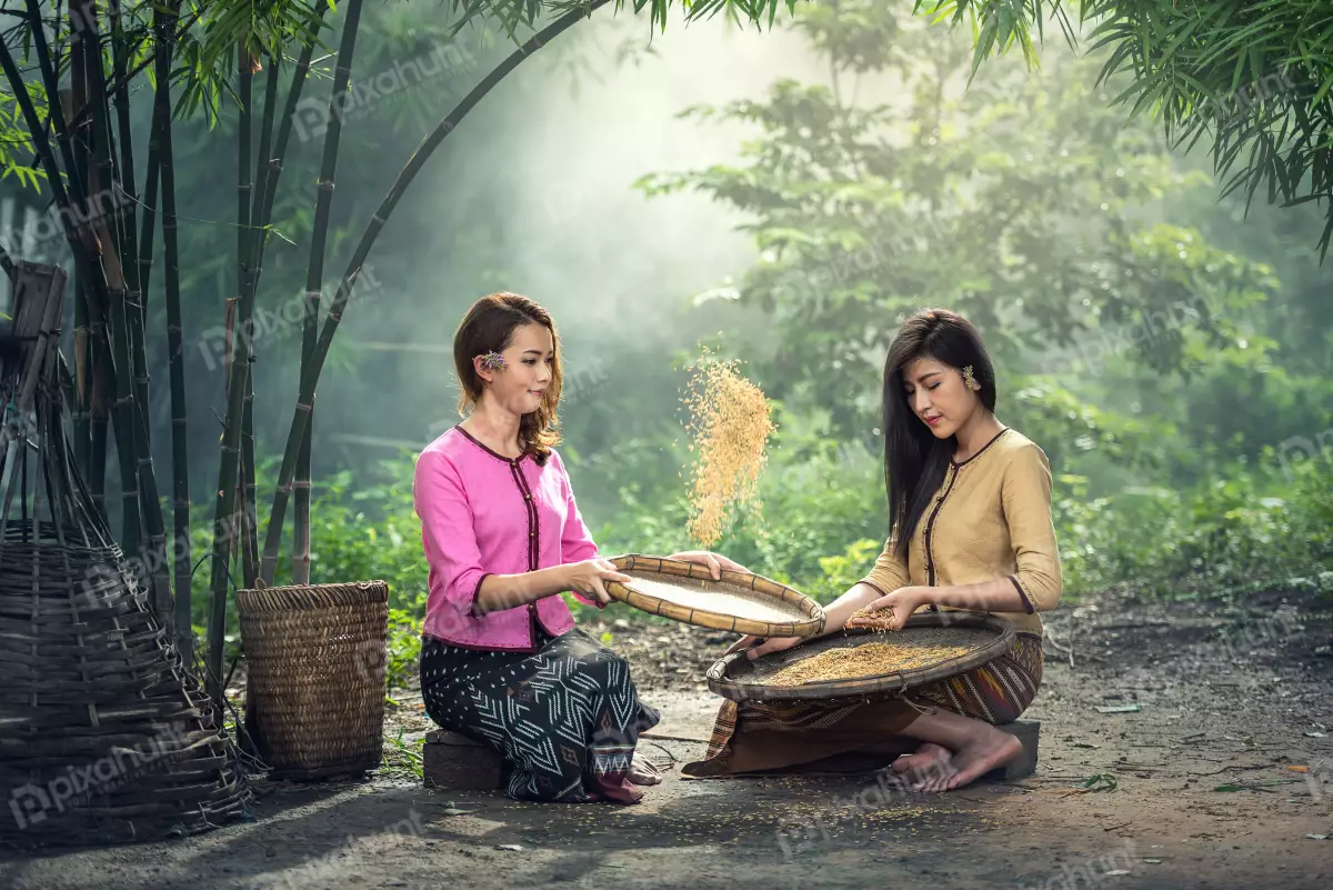 Free Premium Stock Photos Two Girl in traditional clothing sitting on the ground and winnowing rice