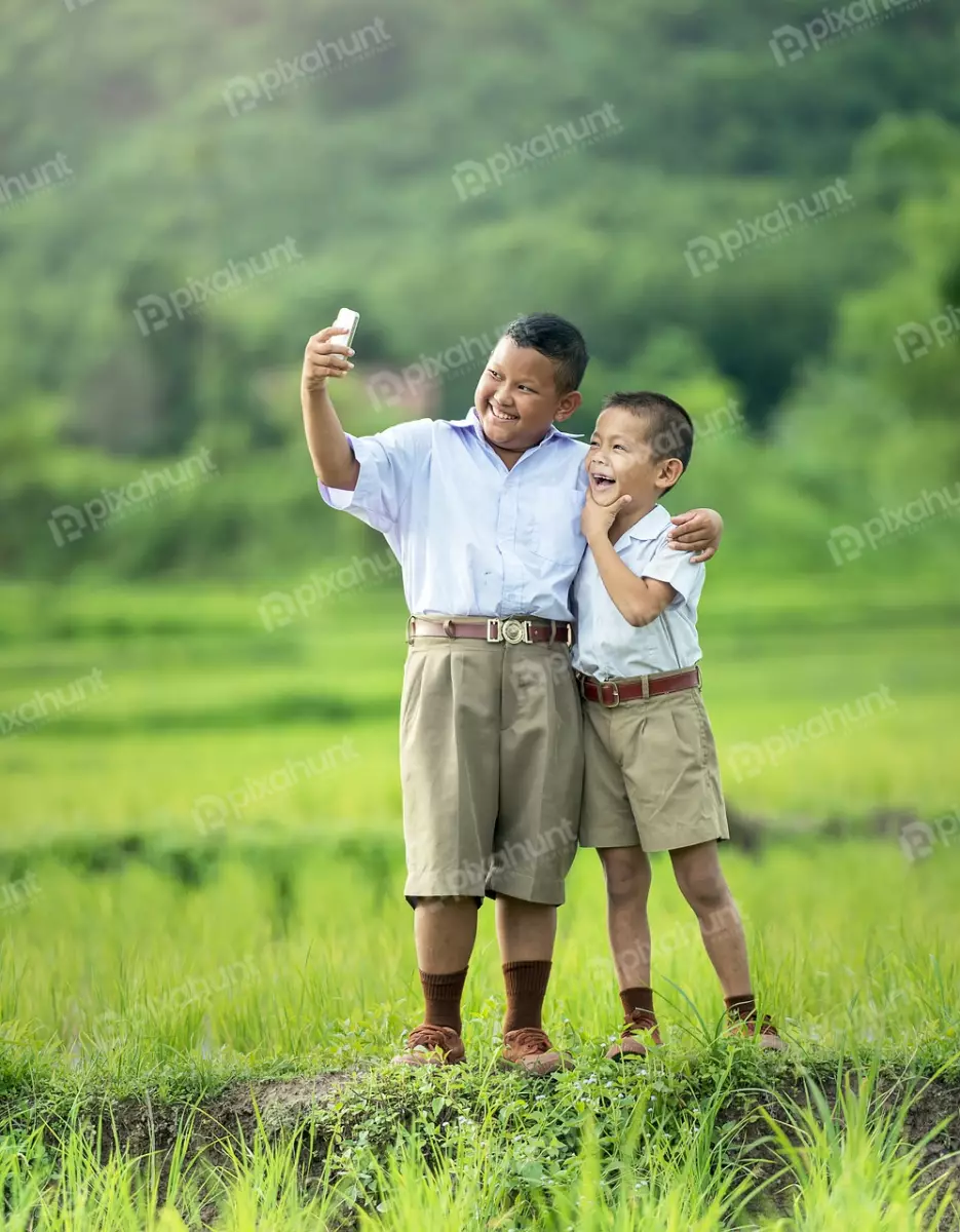Free Premium Stock Photos Two school boys standing in a grassy field and take selfie and standing close together with one boy's arm around the other's shoulder