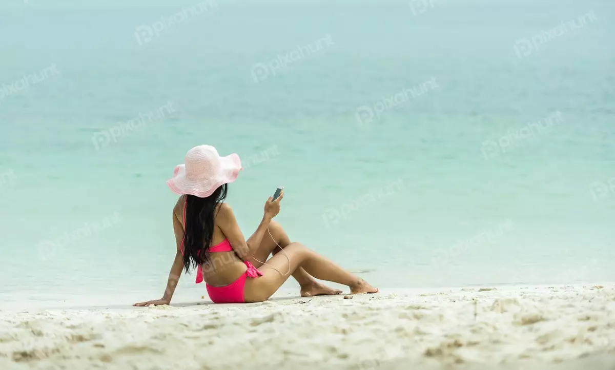 Free Premium Stock Photos Woman is sitting on the sand with her back to the camera and head is turned to the side, and she is looking at her phone