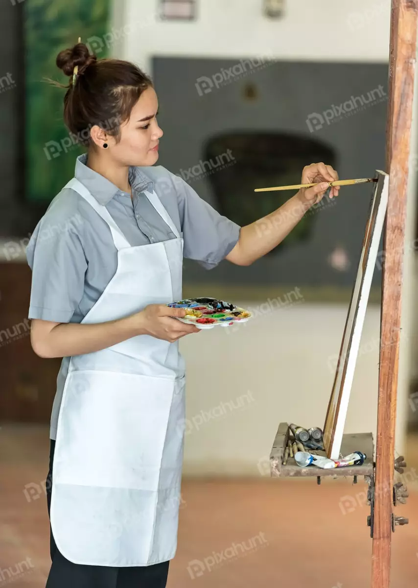 Free Premium Stock Photos Woman painting on a canvas and wearing a white apron and has her hair in a bun