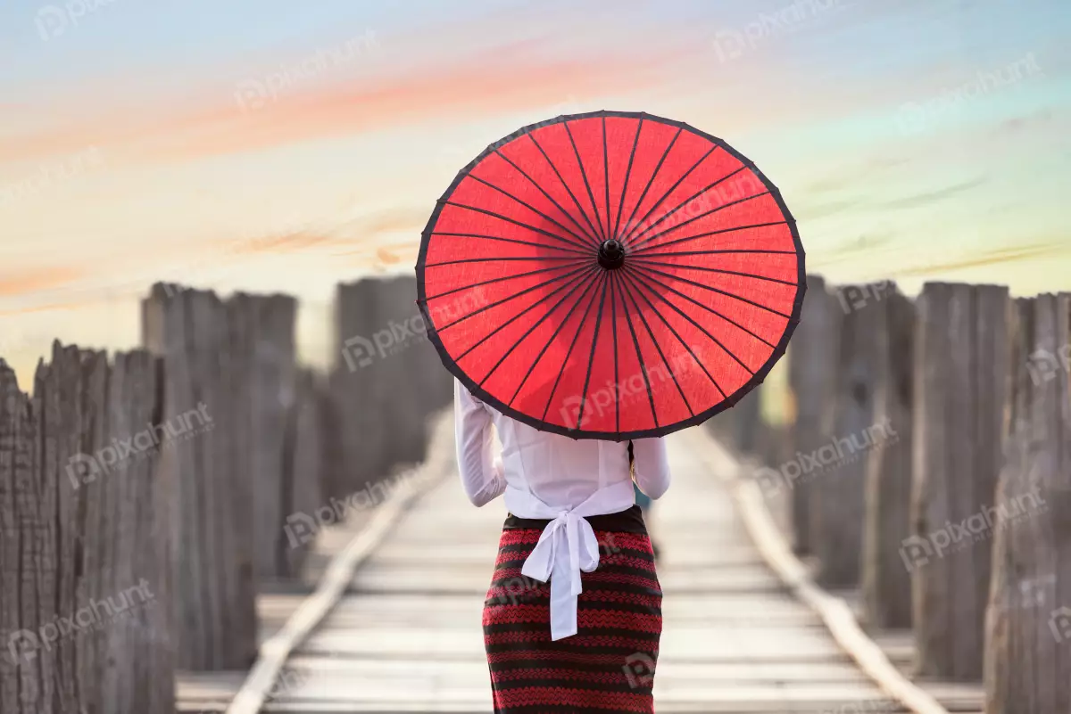 Free Premium Stock Photos Woman standing on a wooden bridge and girl is wearing a traditional Burmese longyi and a red parasollooking up at a woman standing on a wooden bridge. The woman is wearing a traditional Burmese longyi and a red parasol