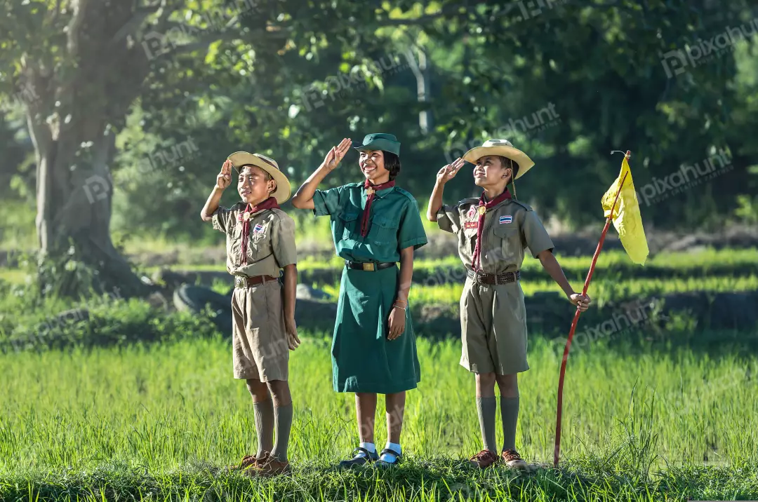 Free Premium Stock Photos Three scouts in a field, saluting and two boys are wearing brown uniforms, and the girl is wearing a green uniform