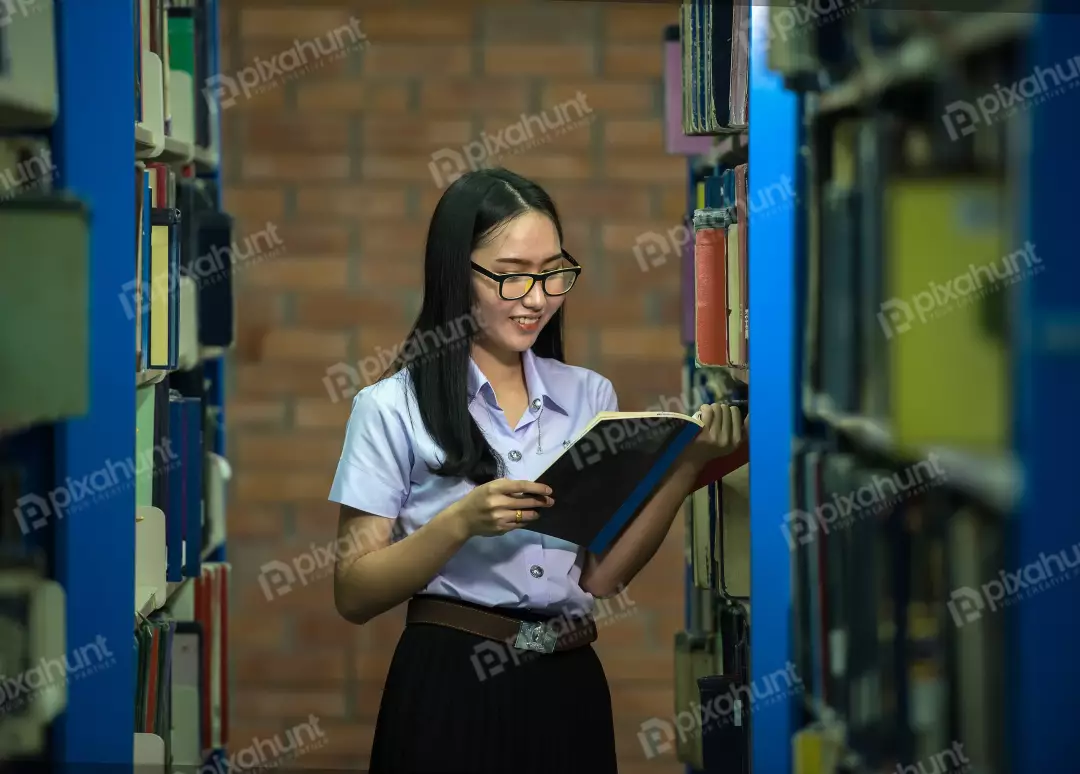 Free Premium Stock Photos A young girl standing in a library, looking at a book and wearing a white shirt, black skirt, and glasses