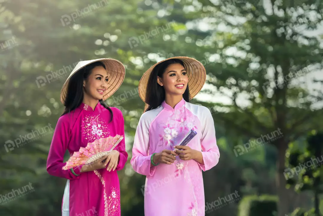 Free Premium Stock Photos Two Vietnamese women wearing traditional ao dai dresses and both smiling and holding fans