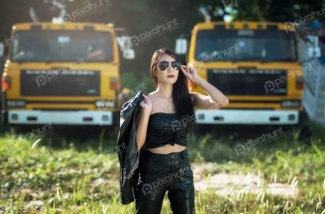 Free Premium Stock Photos A woman in a black leather jacket and sunglasses stands in front of two yellow trucks And looking at the camera and has one hand on her hip and the other holding her jacket