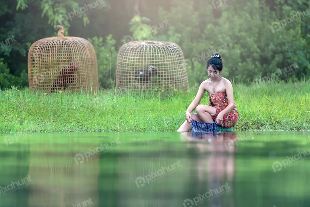 Free Premium Stock Photos A young girl in a traditional Thai outfit sitting on the edge of a river and washing clothes in the water