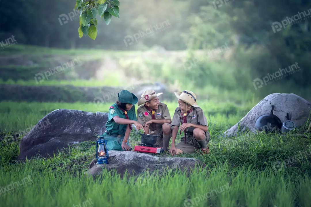 Free Premium Stock Photos Three boy scouts in a forest and gathered around a campfire and one of them is stirring a pot of food