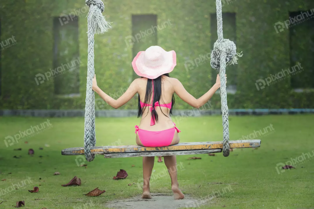 Free Premium Stock Photos Girl is wearing a wide-brimmed hat that shades her face from the sun And  sitting on a wooden swing, which is suspended from two thick ropes