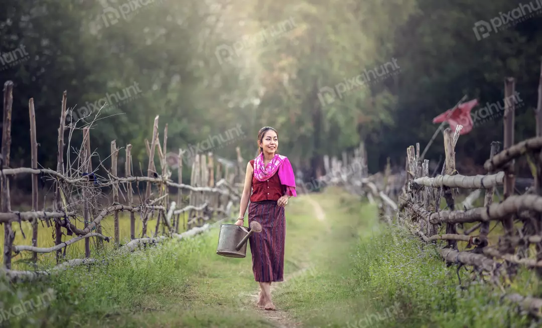 Free Premium Stock Photos A woman in a traditional Hmong outfit and walking down a path in a rural area carrying a watering can