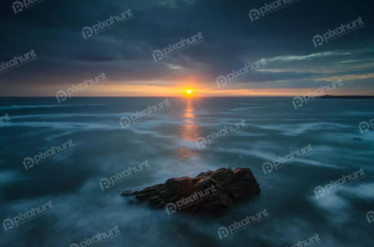 Free Premium Stock Photos looking out at a large rock in the middle of the ocean with rock is surrounded by water and the waves are crashing against it