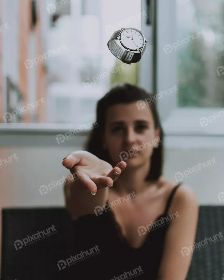 Free Premium Stock Photos a young woman in a black dress sitting on a couch and looking at a watch that is in the air