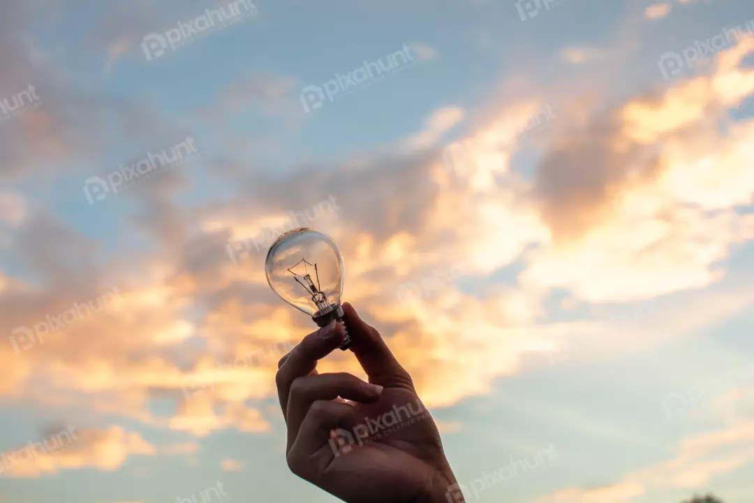 Free Premium Stock Photos A hand holding a light bulb with a sunset in the background