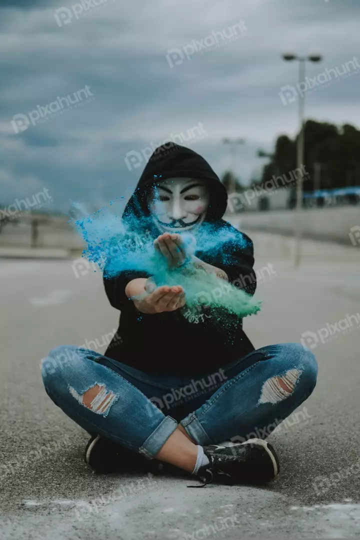 Free Premium Stock Photos A person wearing a Guy Fawkes mask sitting on the ground with a colorful powder in their hands