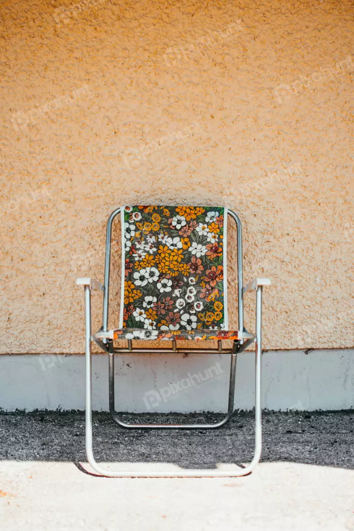 Free Premium Stock Photos a vintage floral pattern lawn chair sitting at an angle in front of a yellow wall