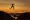 A low angle, looking up at a woman who is jumping over a large rock