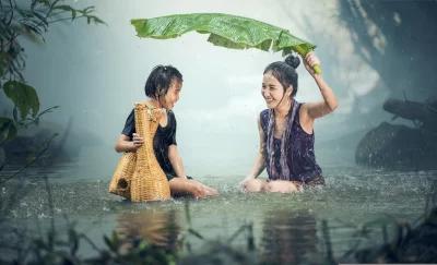 Mother and her child is holding a banana leaf over her head to protect them from the rain