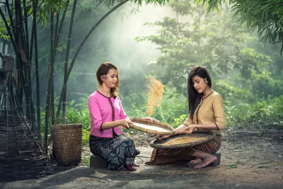 Two Girl in traditional clothing sitting on the ground and winnowing rice