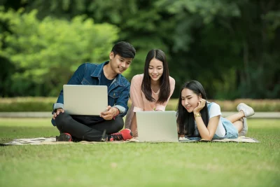 Three people sitting on the grass in a park and they are all looking at their laptops